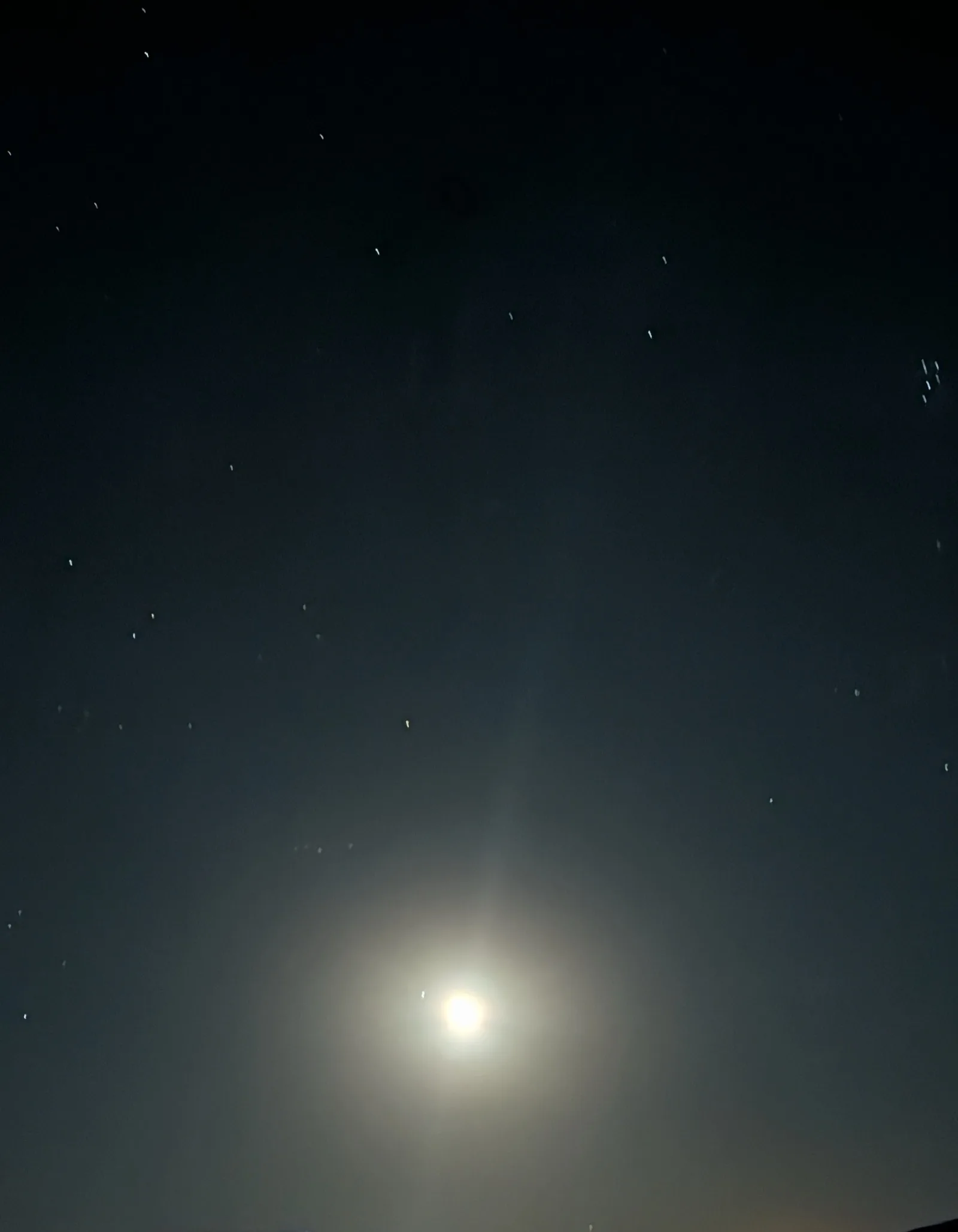 The moon glowing low in a dark desert sky, stars streaking faintly above it.